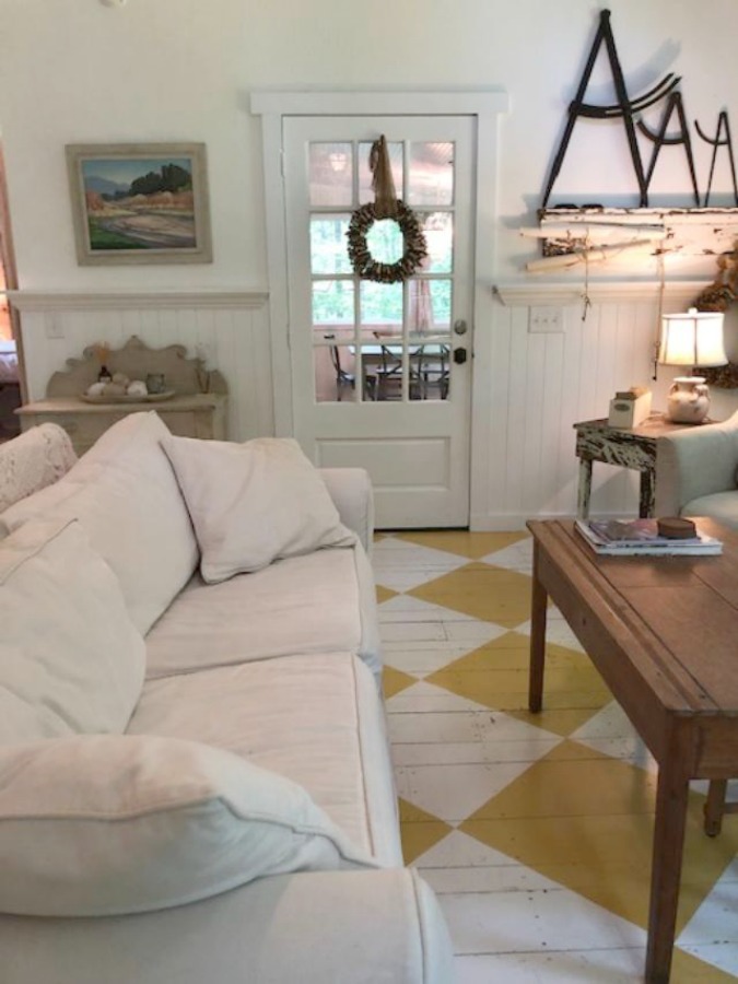 Farmhouse chic living room with vintage treasures, bold yellow painted poplar wood flooring, linen upholstery, and design by City Farmhouse for Storybook Cottage in Leiper's Fork, TN - Hello Lovely Studio. #farmhousestyle #livingroom #cityfarmhouse #storybookcottage