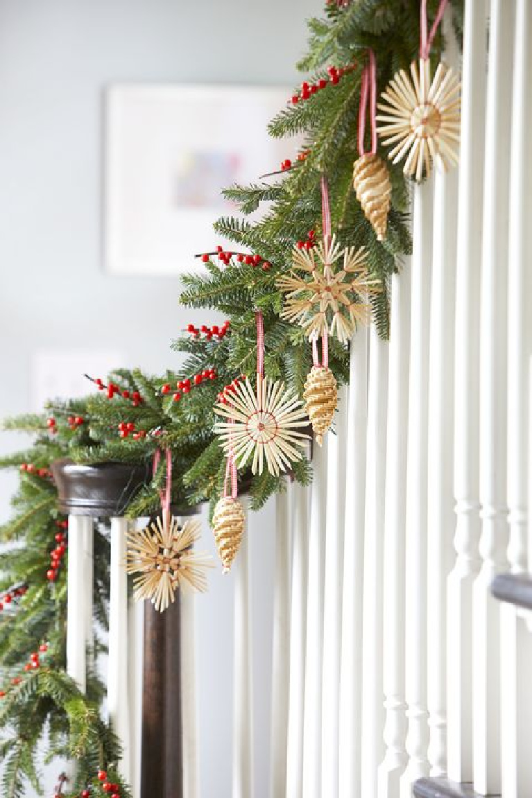 Charming Scandinavian Christmas straw ornaments and fresh garland on white staircase in a cottage style home.