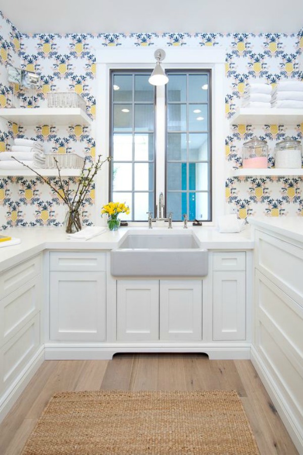 Farm sink, cheerful wallpaper, floating shelves, and white custom cabinetry in a butler pantry of a modern French home. #butlerpantry #floatingshelves #frenchcountry #farmsink