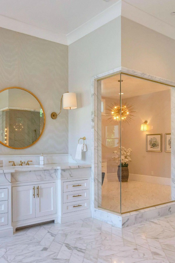 Luxurious bath design with marble, white cabinetry, and brass hardware in a modern French home in Queen Creek, AZ. #bathroomdesign #luxurious #whitemarble #modernFrench