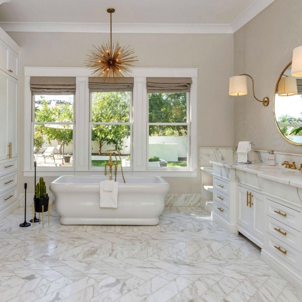 Luxurious bath design with marble, white cabinetry, and brass hardware in a modern French home in Queen Creek, AZ. #bathroomdesign #luxurious #whitemarble #modernFrench