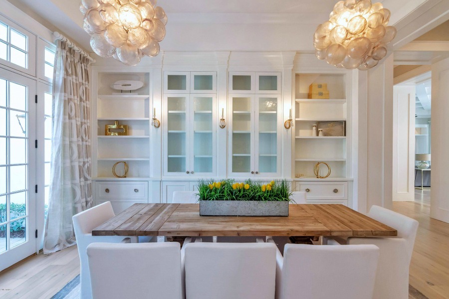 Modern French interior design in a dining room with contemporary pendants, built-ins, and a rustic dining table. #modernfrench #interiordesign #diningroom #builtins