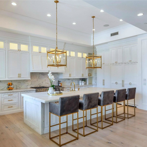 Breathtaking white kitchen with farm sink and large island with brass hardware in modern French home. #interiordesign #kitchendesign #modernfrench #whitekitchen