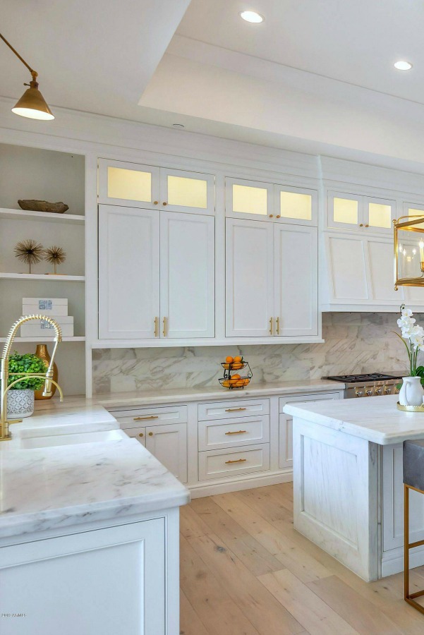 Breathtaking white kitchen with farm sink and large island with brass hardware in modern French home. #interiordesign #kitchendesign #modernfrench #whitekitchen