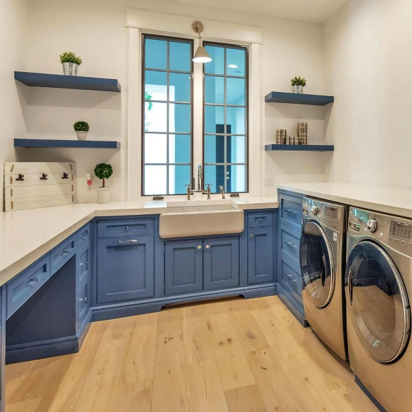 Modern French laundry room with bright blue painted cabinetry, floating shelves, and farm sink. #laundryroom #interiordesign #modernfrench #bluecabinets