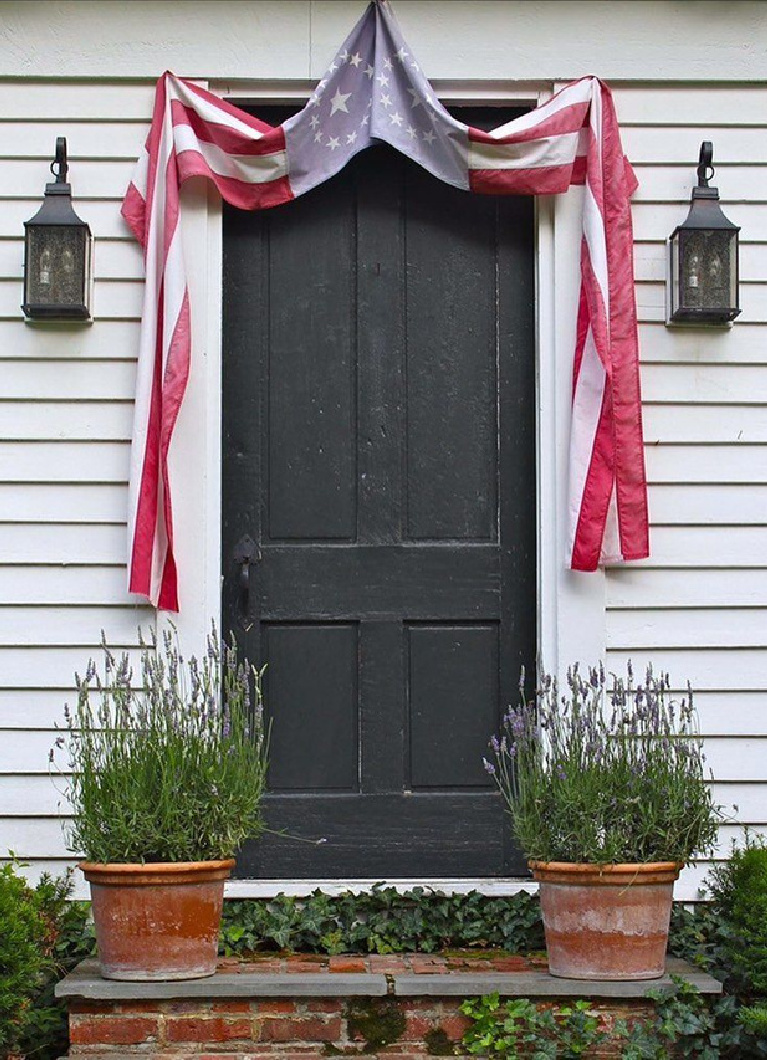 Nora Murphy's charming Connecticut farmhouse black door with faded American flag bunting and old lanterns flanking it. #noramurphy #farmhousedoor #4thofjuly #countryhouse #americana #countrystyle