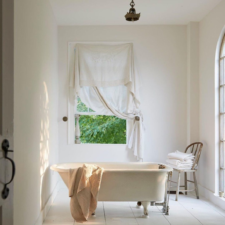 A charmingly serene white French country bath with white painted floors, clawfoot tub, magnificent naturallight and vintage textiles. Wendy Lewis design (Textile Trunk) featured in Nora Murphy's Country House book (Vendome Press).