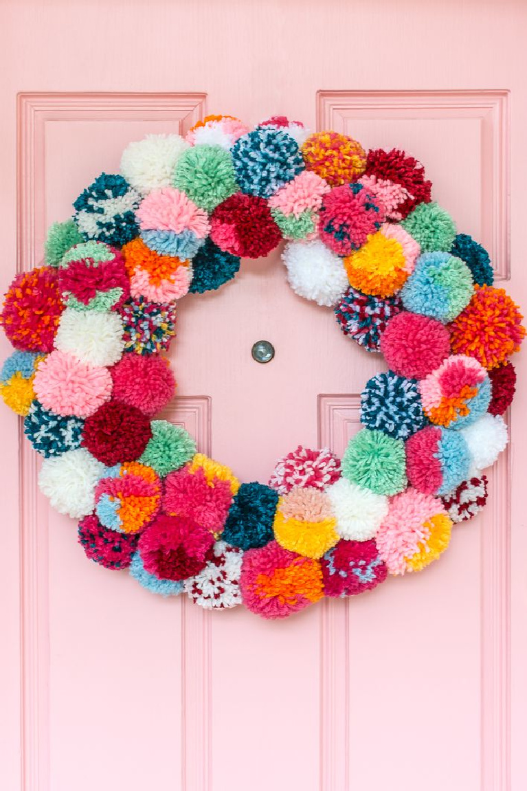 Darling colorful boho popm pom Christmas wreath on a candy pink door for the holidays - Rachel Jacks/Curbly.