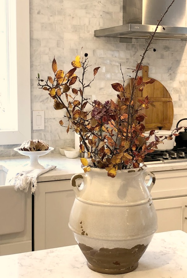 Tuscan style terra cotta urn with golden leafy branches in Shaker style white cabinets in simple serene kitchen. Viatera Minuet quartz countertops - Hello Lovely Studio.
