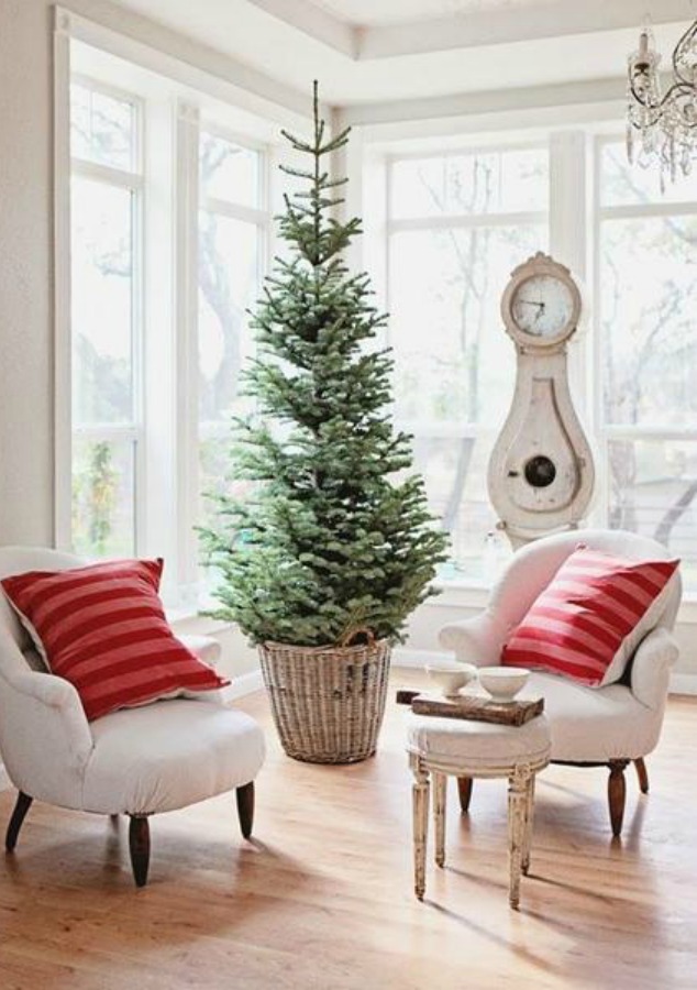 French farmhouse Christmas decor in a living room by Dreamy Whites with Swedish mora clock, tree in vintage basket, and pink stripe pillows. #farmhousechristmas #frenchfarmhouse #holidaydecor #frenchnordicstyle