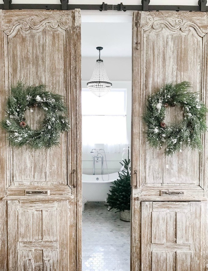 Rustic farmhouse sliding barn doors with Christmas wreaths at entrance to a lovely bath with clawfoot tub - Beside the Mulberry Tree. #farmhousechristmas #christmasdecor #rusticchristmas #countrychristmas #barndoors