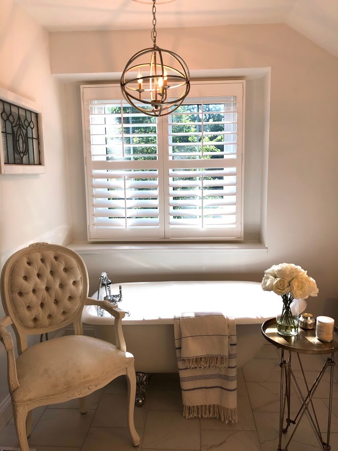 European country inspired white bathroom with clawfoot tub and Louis style chair - Hello Lovely Studio.