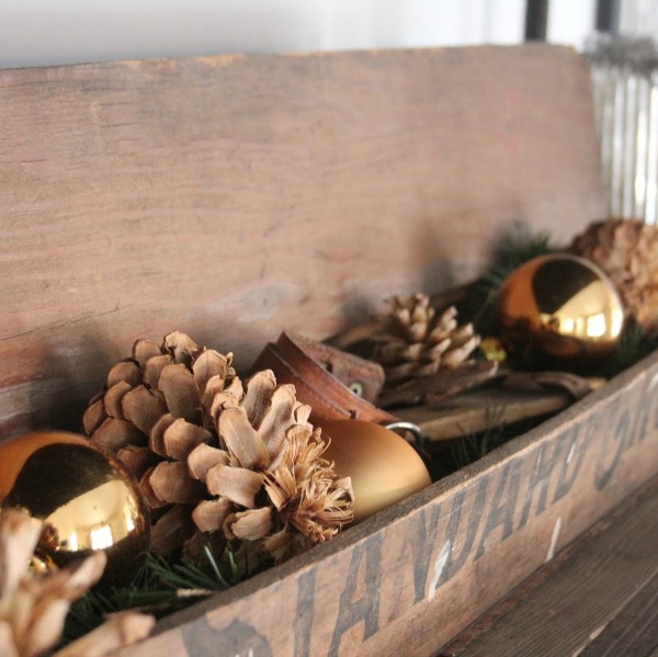 Boîte en bois vintage rustique remplie de pommes de pin et de boules de Noël dorées - Hello Lovely Studio.