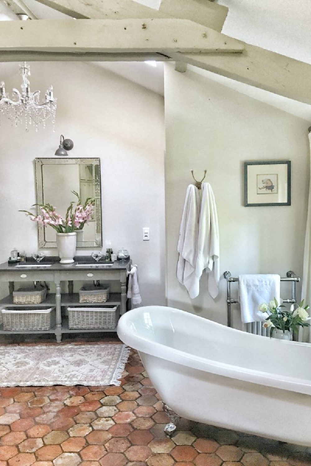 Quiet and timeless hues in a French farmhouse bathroom by Vivi et Margot features reclaimed terracotta hex tiles, freestanding tub, romantic chandelier, and Farrow and Ball's Strong White on the walls.