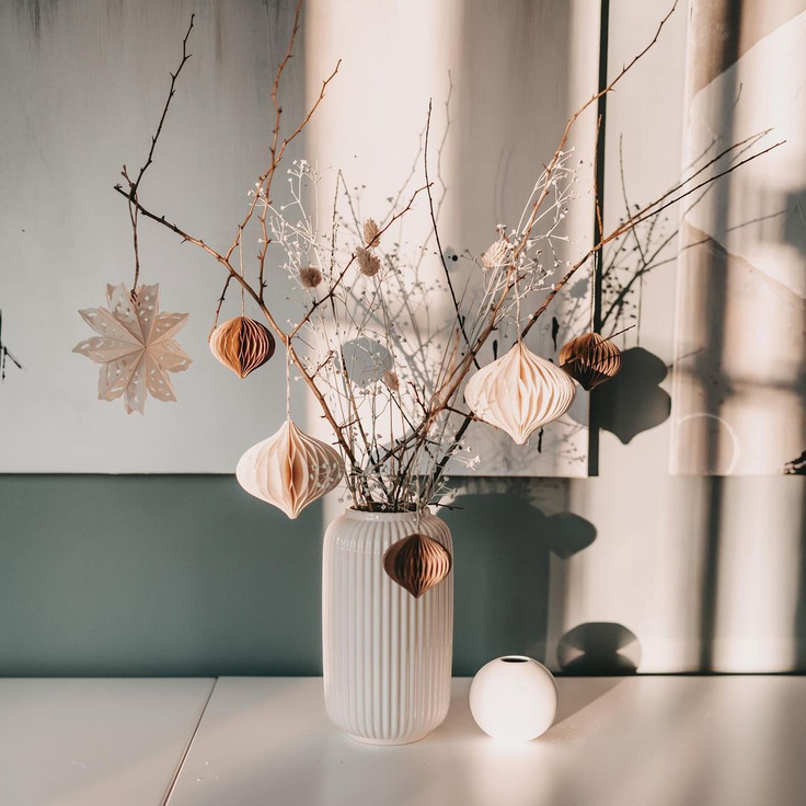 Lovely handmade paper Scandi ornaments dangle from bare branches in a vase for this holiday moment by Herzenseinrichtung.