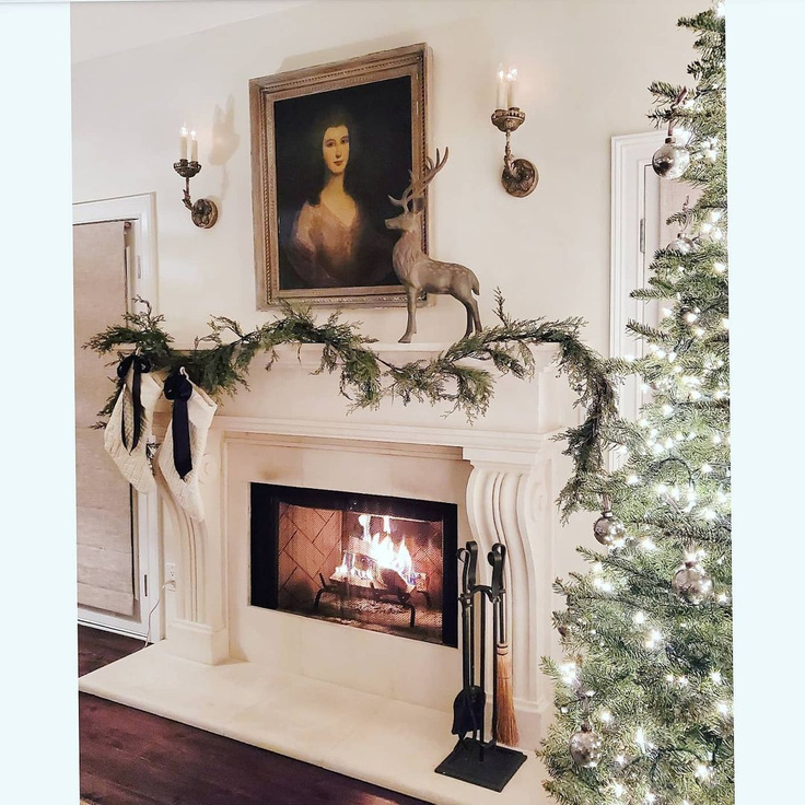 Elegant French country Christmas decorated living room with fireplace, portrait, stag, greenery, and white stockings - TheFrenchNestCoInteriorDesign.