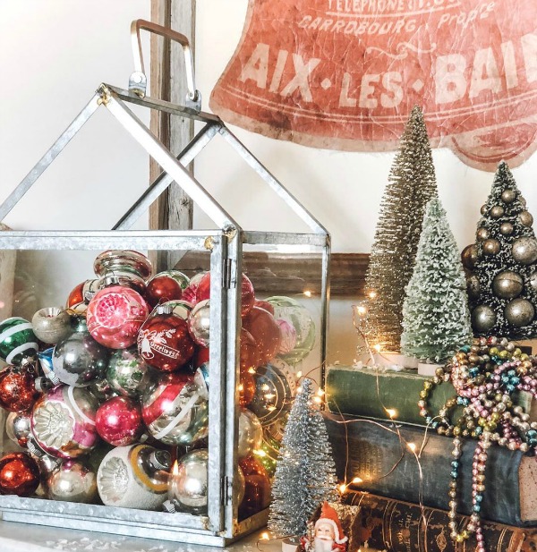 Vintage Christmas and farmhouse holiday decor with ornaments in a glass lantern and bottle brush trees - Le Cultivateur. Come find more Christmas Decorating Ideas to PIN for Happy Holidays. #christmasdecor #farmhousechristmas #vintagechristmas #holidaydecor