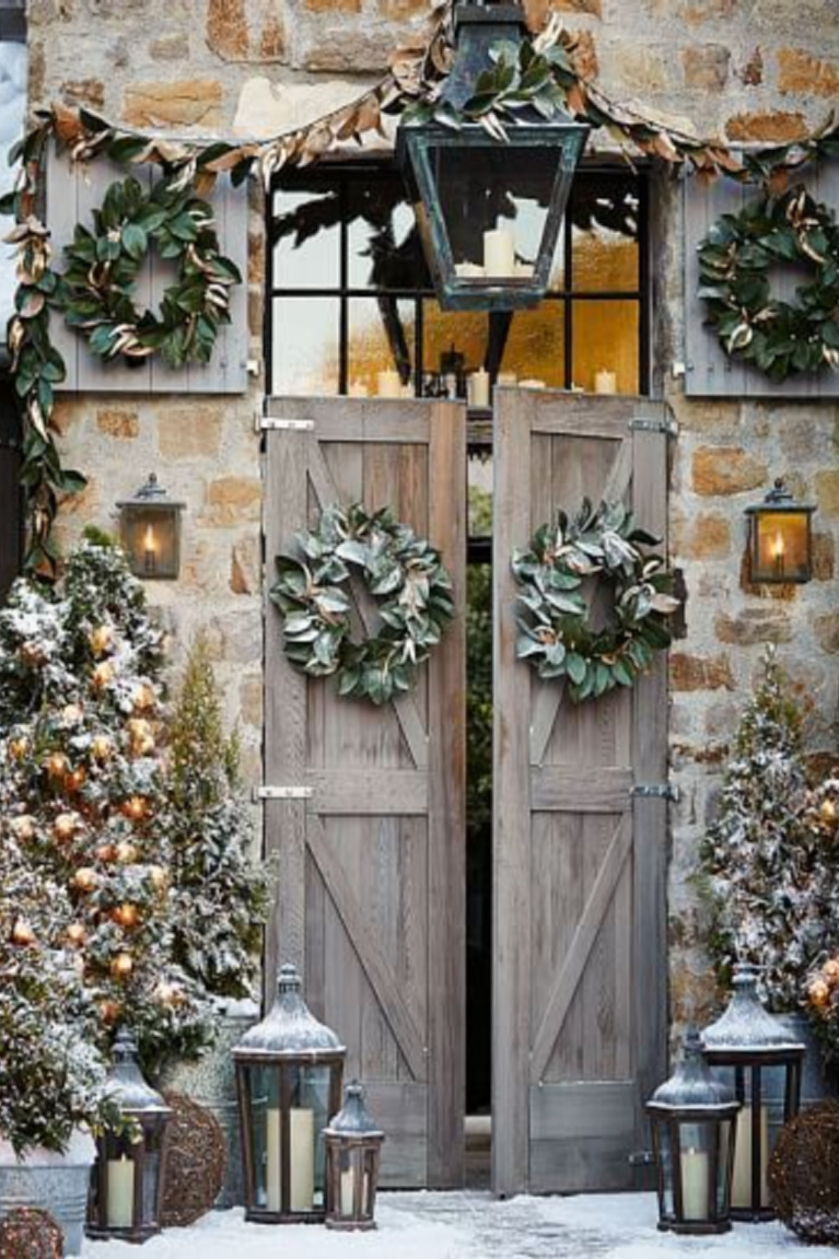Christmas decoor on a charming stone barn with rustic wood doors, Christmas wreaths, and lanterns - Pottery Barn.
