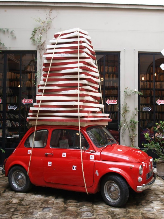 Vintage European red tiny car piled high with packages in front of Merci boutique in Paris - Hello Lovely Studio. #merciboutique #parisshop #vintagecar #redcar