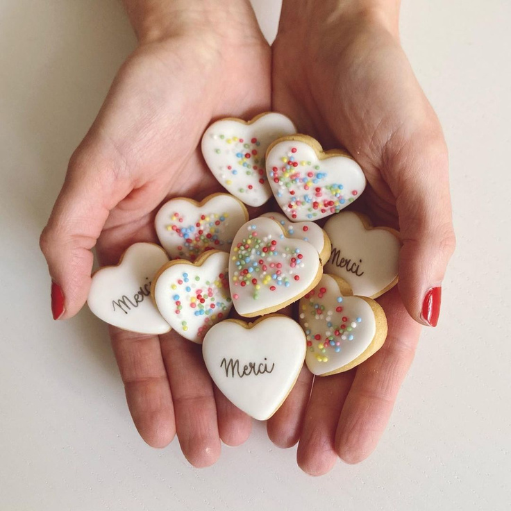 Tiny frosted heart cookies with sprinkles and "merci" in hands - @biscuitz_biarritz.