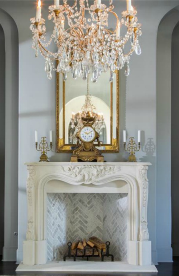 Elegant French mantel and crystal chandelier in a Houston mansion with French country design. #frenchfireplace #oldworldstyle #interiordesign #frenchcountry