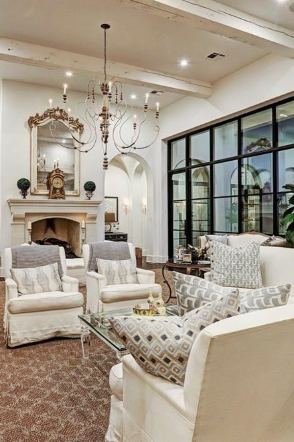 Luxurious white French country living room with black steel windows and French fireplace. #frenchcountry #livingroom #interiordesign #luxuryhome