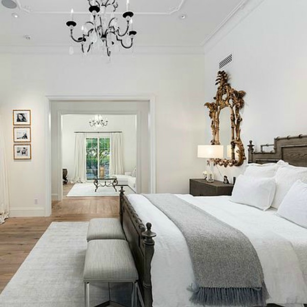 Beautiful white luxurious French bedroom with gallery white walls, gilded mirror, and sitting area. #bedroomdesign #whitebedroom #frenchcountry #interiordesign