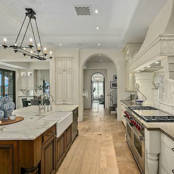 Elegant French country kitchen in luxurious Scottsdale home with stone floor, two tone cabinets, farm sink, and arch doorways. #luxuriouskitchen #frenchcountrykitchen #elegantdecor #kitchendesign