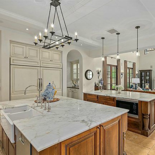 Double islands in elegant French country kitchen in luxurious Scottsdale home with stone floor, two tone cabinets, farm sink, and arch doorways. #luxuriouskitchen #frenchcountrykitchen #elegantdecor #kitchendesign