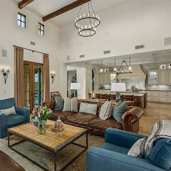 French country great room with brown leather Chesterfield sofa and white kitchen in a luxurious Scottsdale home. #greatroom #interiordesign #luxurioushome 