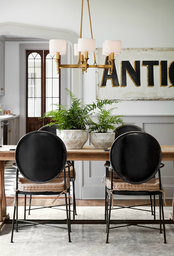 Dining room with modern black chairs, farm table, grey trim, and serene color palette.  Come get inspired by Tranquil and Timeless Tudor Design Details From a Serene 1920s Texas Cottage renovated on HGTV's Fixer Upper by Chip and Joanna and known as the Scrivano House. #fixerupper #scrivano #cottagestyle #interiordesign #greytrim #serenedecor #diningroom #louisdiningchair
