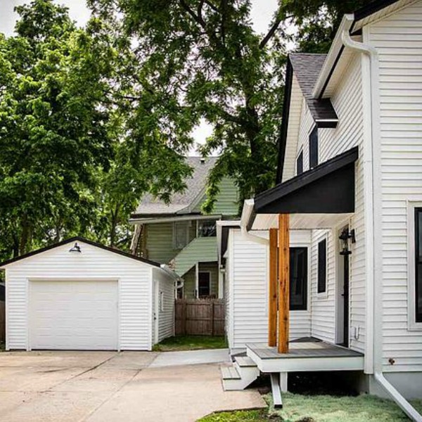 Charming 1900 renovated white urban farmhouse exterior in Beloit, WI with black windows, wood porch columns, and natural wood accents. #hellolovelystudio #urbanfarmhouse #houseexterior #modernfarmhouse #blackwindows