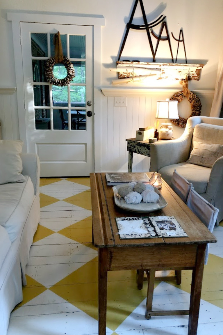 Lovely American country cottage living room in Leiper's Fork, TN, with yellow check wood floor, white decor and vintage, and art by Michele of Hello Lovely Studio.