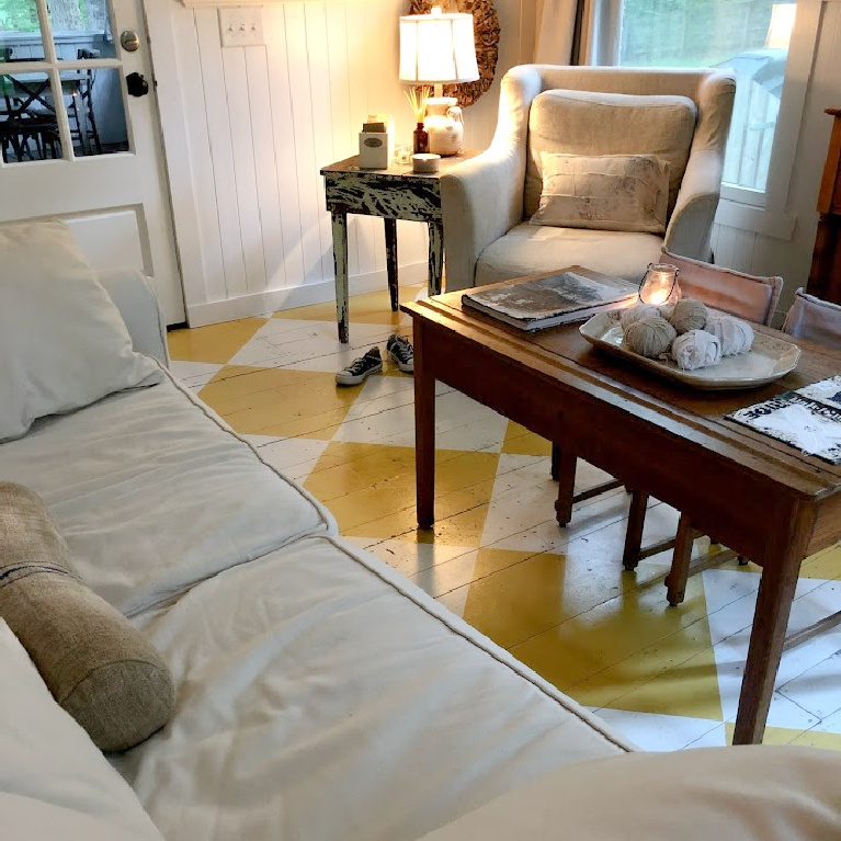 Lovely American country cottage living room in Leiper's Fork, TN, with yellow check wood floor, white decor and vintage, and art by Michele of Hello Lovely Studio.