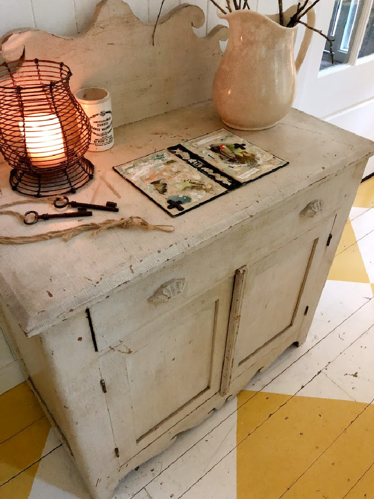 Lovely American country cottage living room in Leiper's Fork, TN, with yellow check wood floor, white decor and vintage, and art by Michele of Hello Lovely Studio.