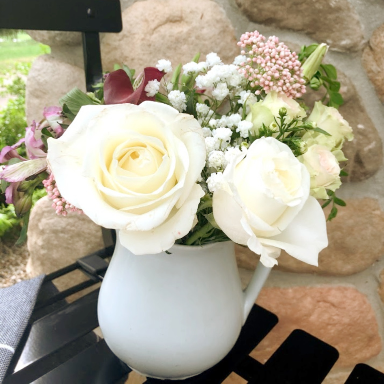 White vintage ironstone pitcher with roses and a summer floral arrangement - on a black Parisian bistro chair in the courtyard - Hello Lovely Studio.