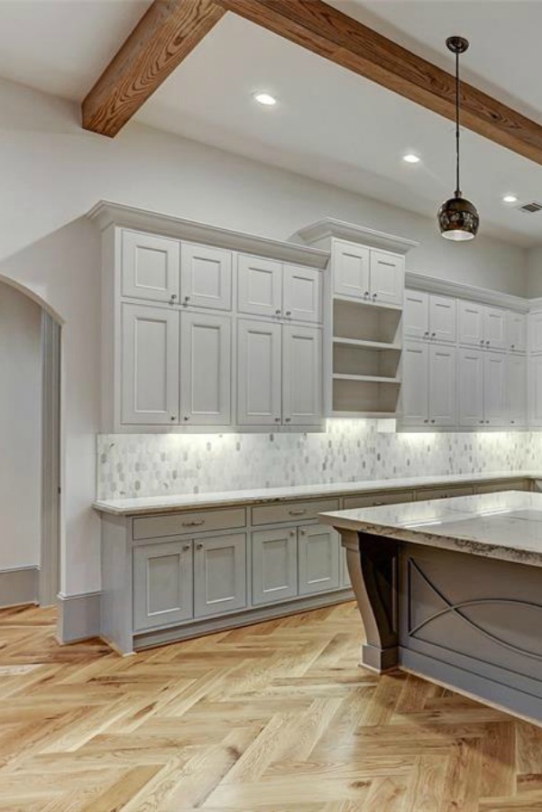 Elegant and sophisticated light grey and white kitchen with ceiling beams and herringbone wood floor. #kitchendesign #frenchcountry #customhomedesign #greycabinets