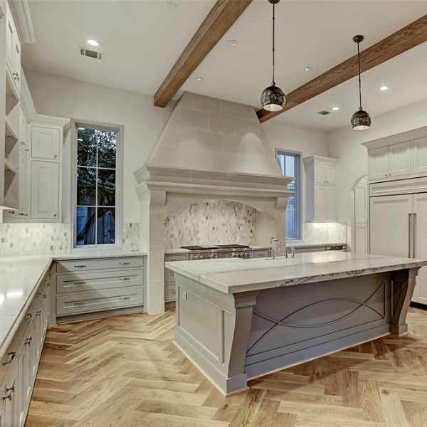 Elegant and sophisticated light grey and white kitchen with ceiling beams and herringbone wood floor. #kitchendesign #frenchcountry #customhomedesign #greycabinets