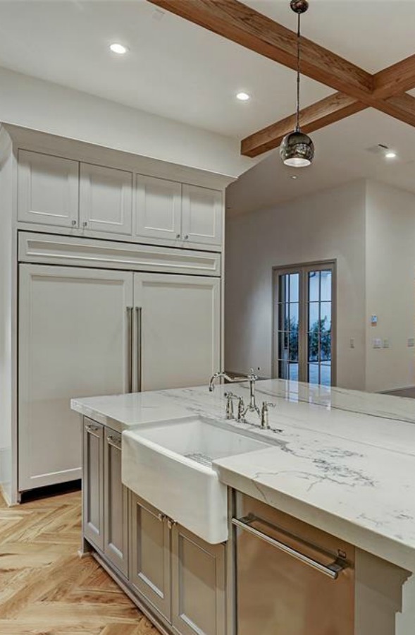 Elegant and sophisticated light grey and white kitchen with ceiling beams and herringbone wood floor. #kitchendesign #frenchcountry #customhomedesign #greycabinets