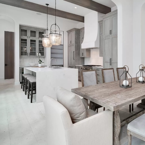 Understated, muted neutrals in a luxurious kitchen and breakfast room of a coastal home (Alys Beach) by Domin Bock. #kitchendesign #warmminimal #luxuriouskitchen #greycabinets #customkitchen