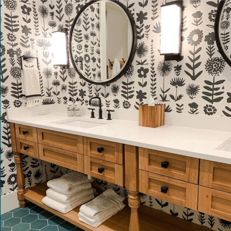 Traditional bathroom design with a fresh twist: black and white bold graphic Schumacher 1889 wallpaper, custom console table style double vanity, round mirrors, and green hex floor tiles. Design by Sherry Hart. #blackandwhite #bathroomdesign #classicstyle #traditionalstyle