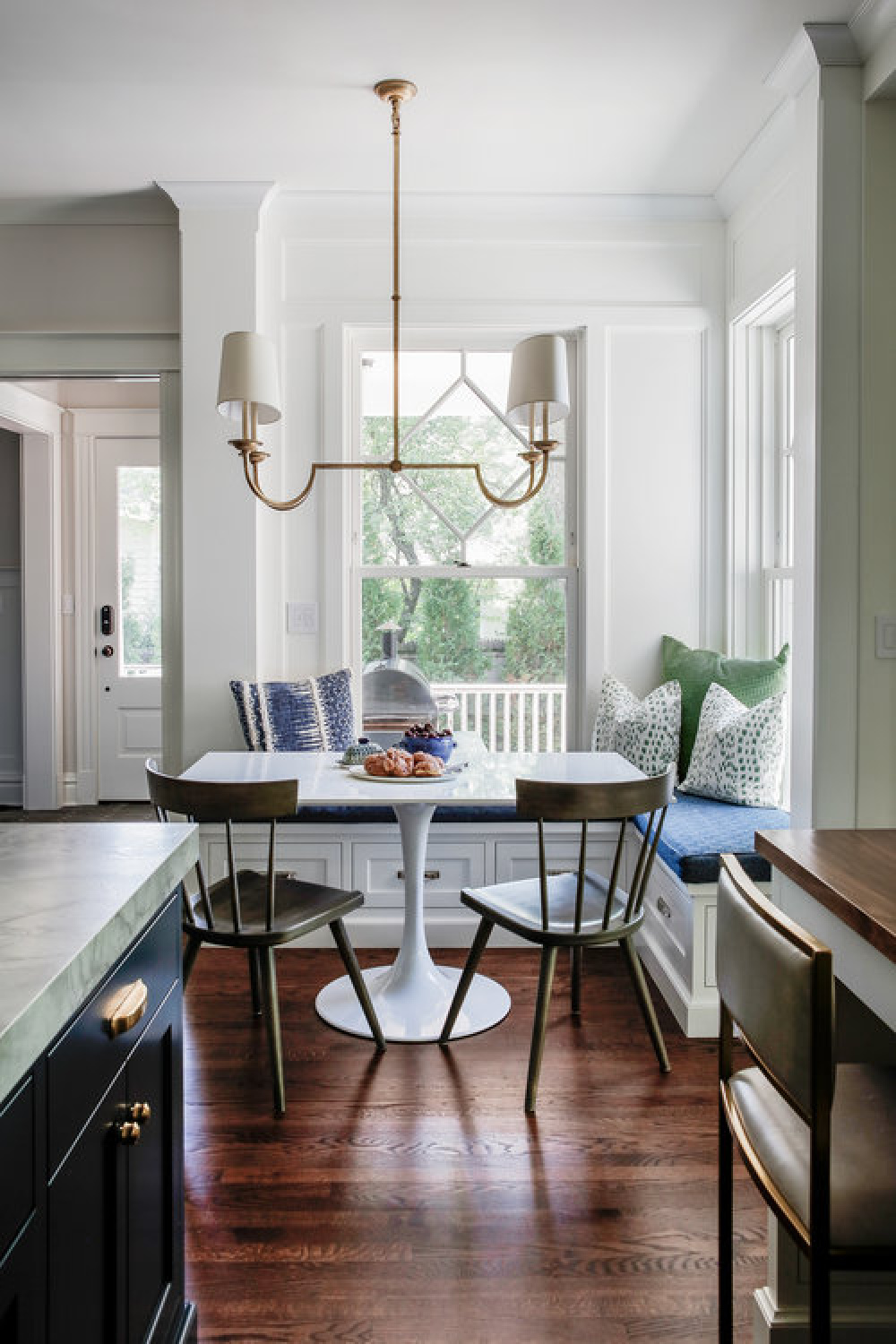 Lovely breakfast nook with built-in window seat and modern Saarinen style table in a blue kitchen by Edward Deegan Architects.