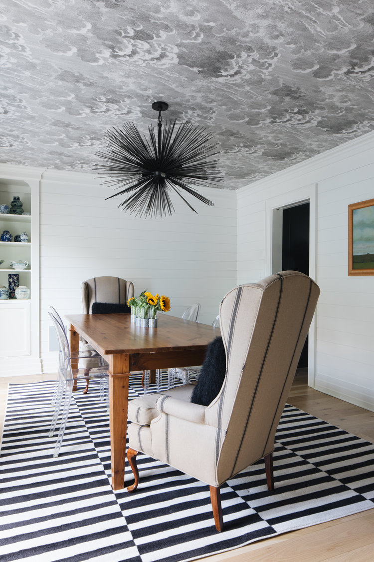 Wallpapered ceiling and black and white stripe rug anchor this eclectic dining room in a modern farmhouse by Edward Deegan Architects. #modernfarmhouse #interiordesign #blackandwhite #diningroom #striperug #wallpaperedceiling