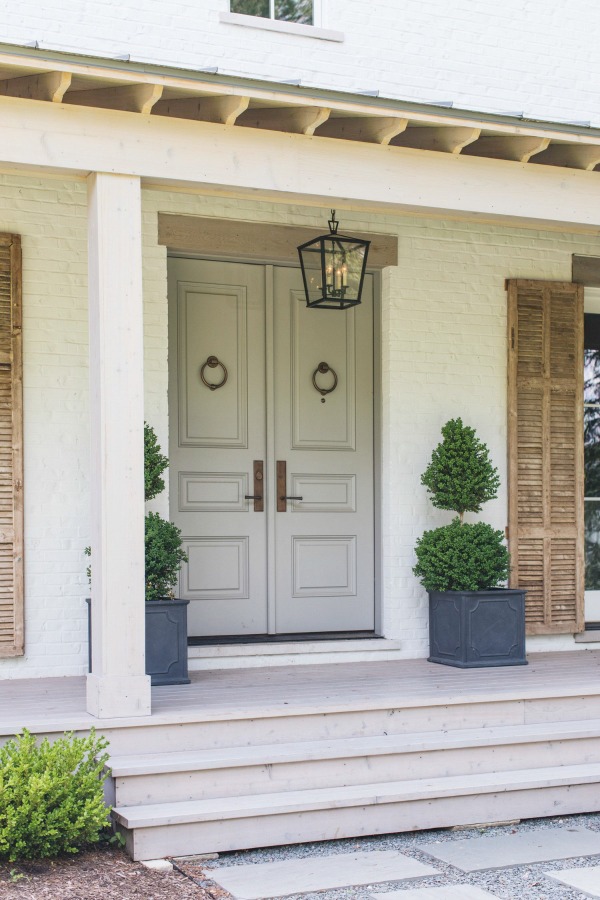 Light grey doors, rustic wood shutters, and white brick on this modern farmhouse exterior work harmoniously - design by Kate Marker in Barrington, IL. Come enjoy encouraging love quotes and timeless decor inspiration! #modernfarmhouse #houseexterior #whitebrick #greydrontdoor