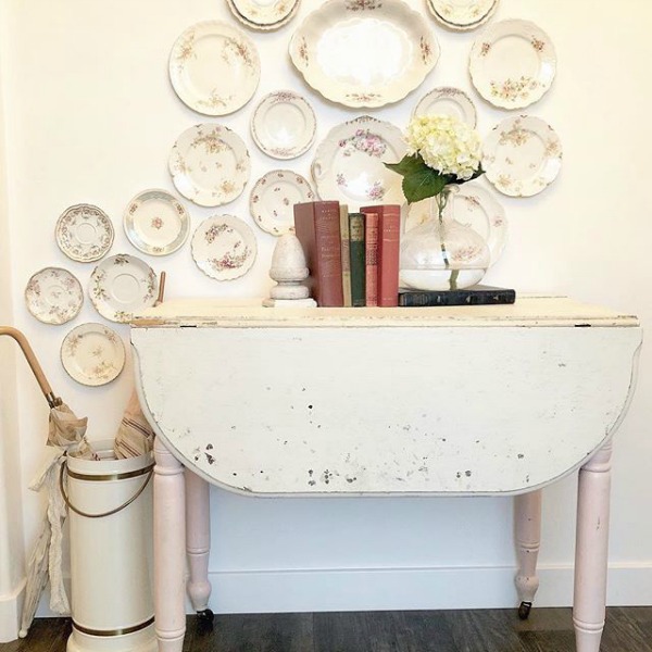 Rustic white country dropleaf table and a collection of vintage plates hung on the wall for a whimsical display by Le Cultivateur. Come see White & Rustic Country Interiors: 19 Ideas to Add Whimsy. #countrydecor #countrystyledecorating #vintageplates #rusticcountrydecor #whitemodernfarmhouse