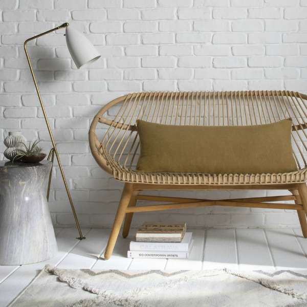 Parachute Home linen lumbar pillow in ochre upon an airy rattan settee with modern floor lamp. #ochrepillow #modernboho #interiordesign