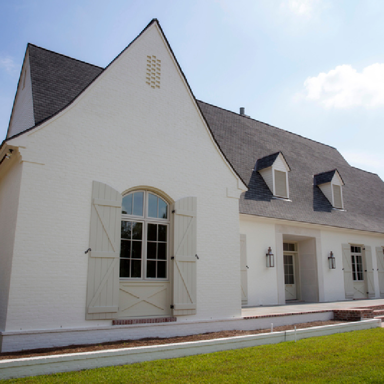 White painted brick Tudor style house with dormers - paint color is Sherwin Williams Original White - shutters are SW City Loft - Telich Custom Homes. #sherwinwilliamsoriginalwhite #paintcolors #houseexteriors