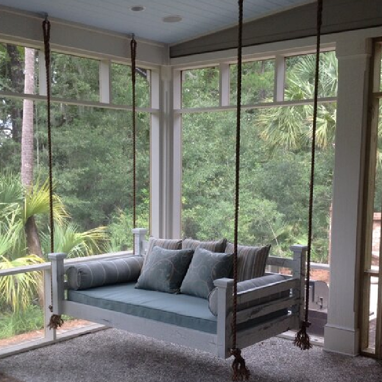 Charleston hanging bed porch swing on a beautiful porch enveloped by lush greenery. #hangingbed #charlestonswing #screenporch #porchdecor #porchfurniture #southernporch