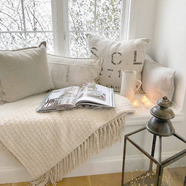 Tone on tone palette at cozy window seat with pillows and candlelight - Hello Lovely Studio. #windowseat #allwhitedecor #scandinavianstyle #interiordesign