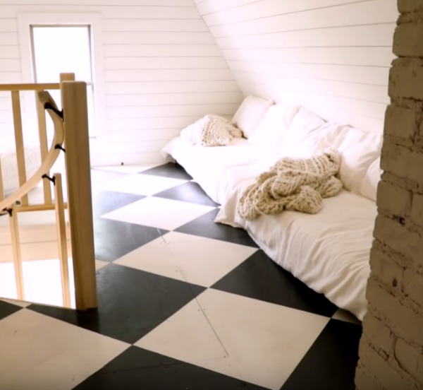 Black and white checkered painted wood floor in an attic with paneled walls and white bedding with cable knit throws. Design by Leanne Ford. #leanneford #whitedecor #blackandwhite #interiordesign